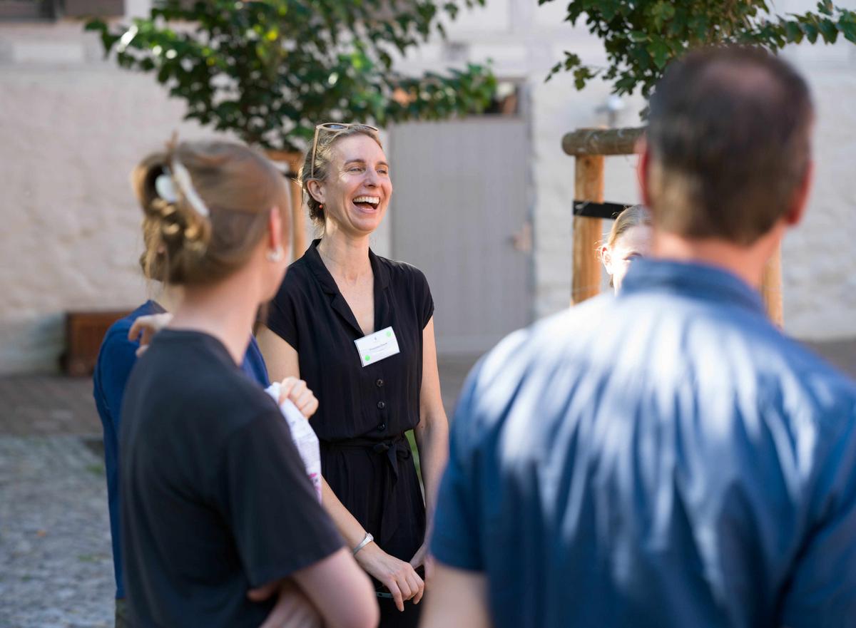 Zwei Personen stehen im Vordergrund und eine Person, die lacht, ist im Hintergrund zu sehen.