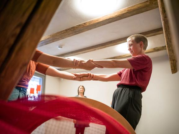 Man sieht eine Person, die von einer anderen, nicht komplett sichtbaren Person, an den Händen bzw. Armen gehalten wird.